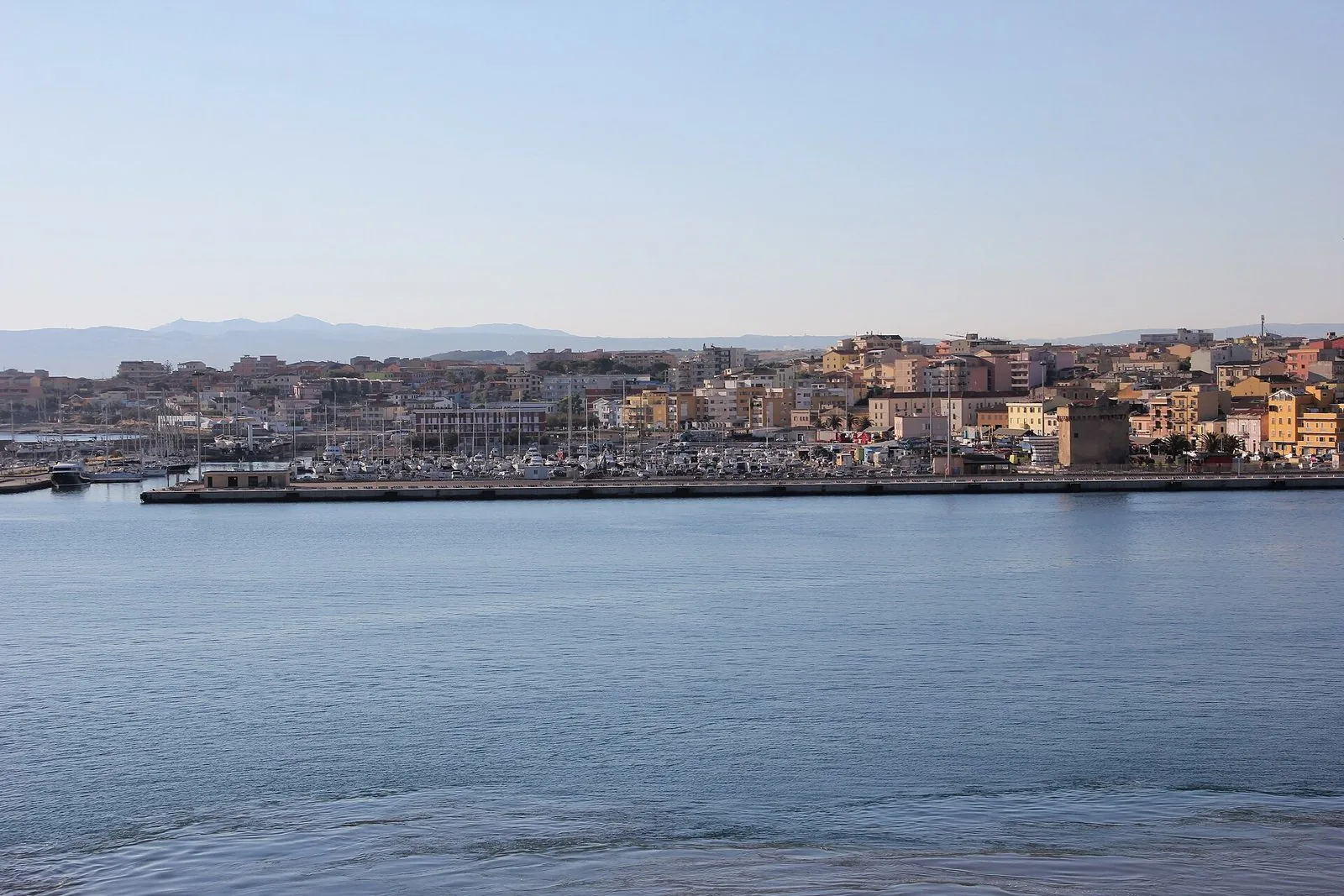 Il porto di Porto Torres visto dal mare, con le barche ormeggiate, le case colorate della città e la torre aragonese sulla destra