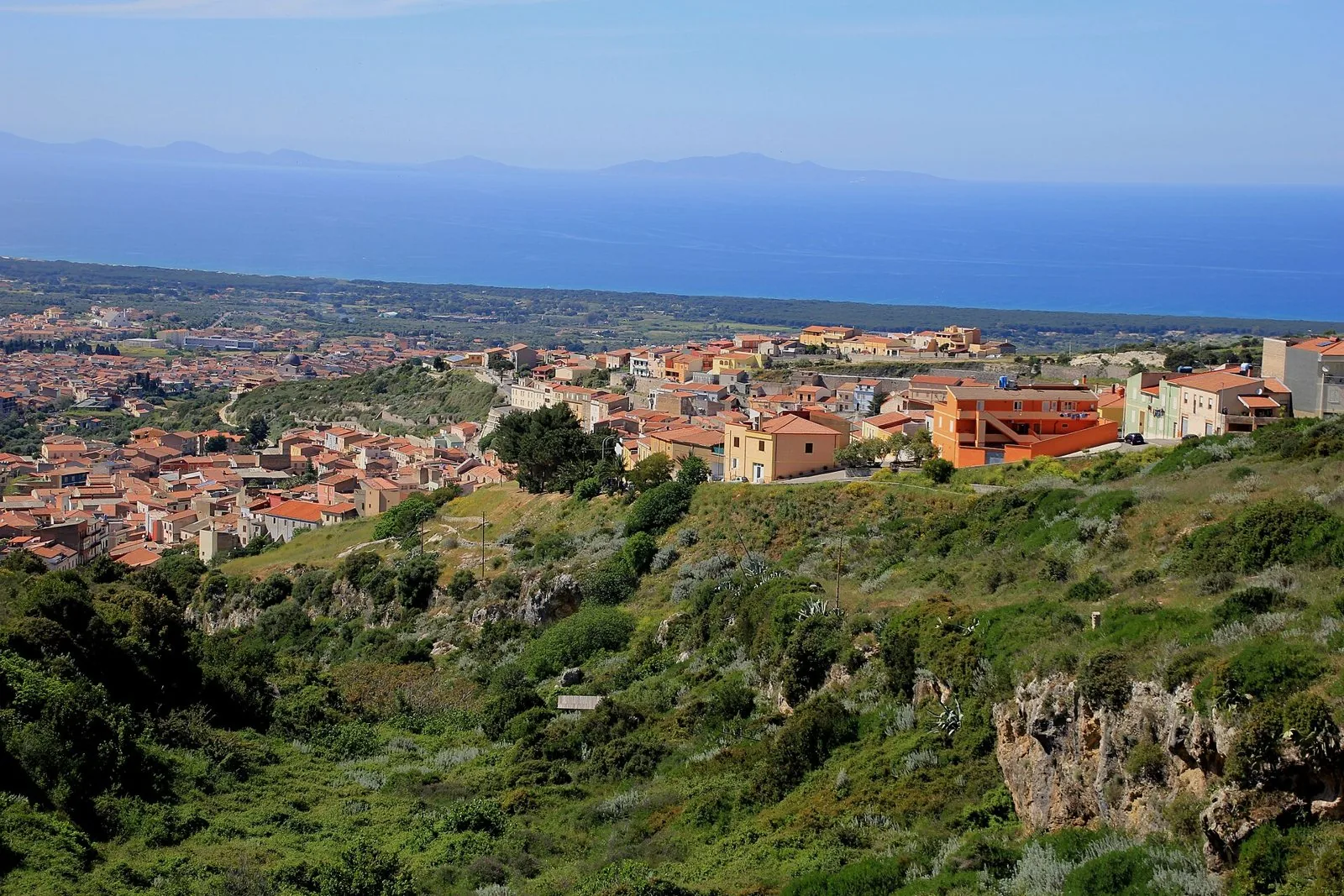 Colline verdi della Romangia con le case di un paese in primo piano e, sullo sfondo, la costa e il golfo dell'Asinara