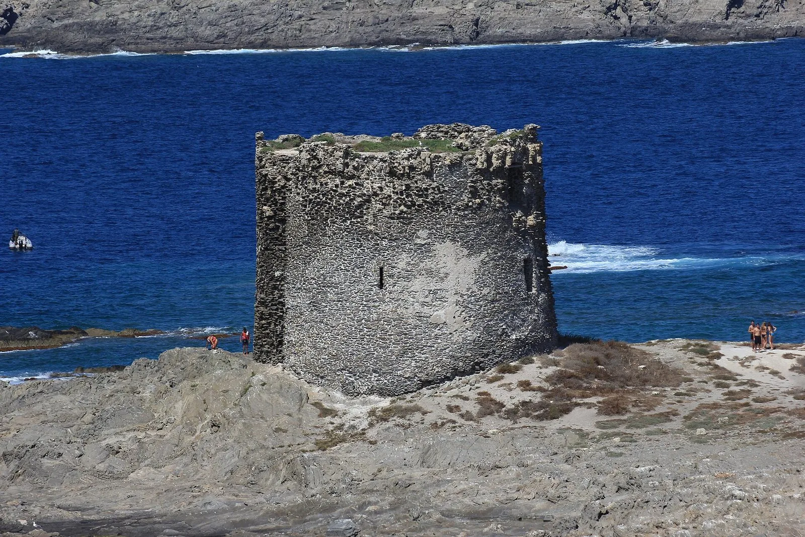 La Torre della Pelosa, torre costiera in pietra sull'isolotto roccioso davanti alla spiaggia, con il mare blu e la costa dell'isola Piana sullo sfondo